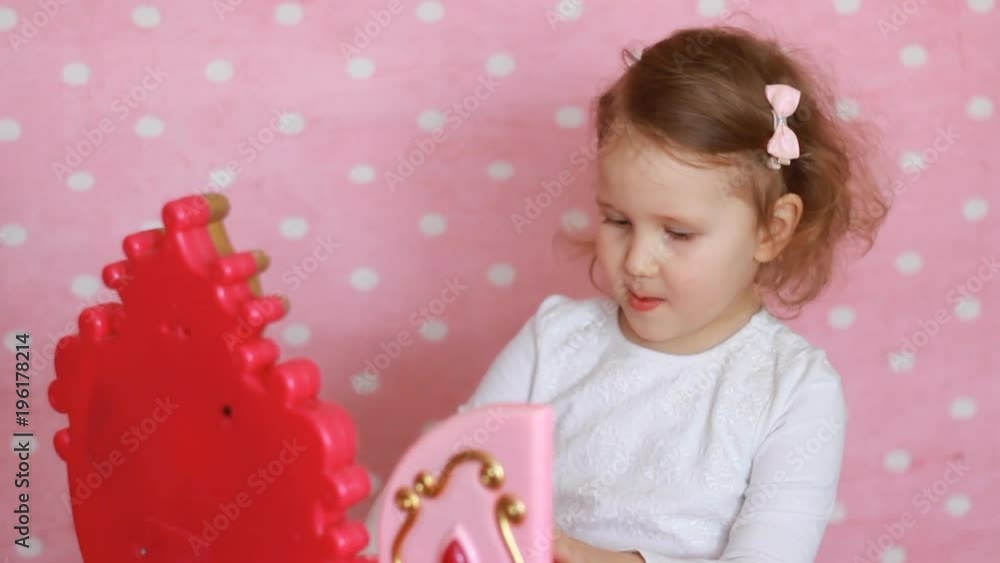 Beautiful little girl looking in the mirror and combs the hair with a wooden comb. A cute child fashionista plays a real lady. Pink background. Glamor Beautiful little girl looking in the mirror and combs the hair with a wooden comb. A cute child fashionista plays a real lady. Pink background. Glamor