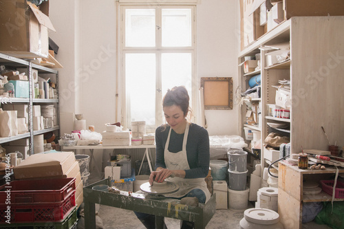 Caucasian woman is shaping pottery clay on a pottery wheel in a ceramic workshop.