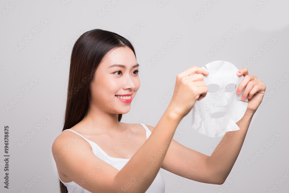 Beautiful asian woman applying paper sheet mask on her face white background. Beautiful asian woman applying paper sheet mask on her face white background.
