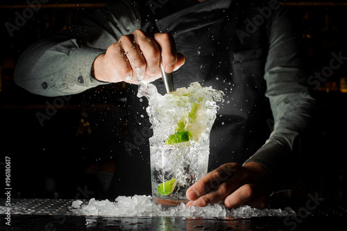 Bartender squeezing juice from fresh lime using a citrus press and splashing it out