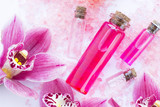 Spa and wellness setting with orchid and rose sea salt and bottle with aroma oil on wooden white background closeup