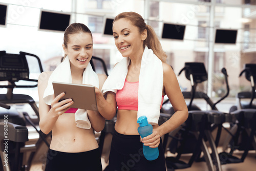 Mother and daughter using tablet at the gym. They look happy, fashionable and fit.