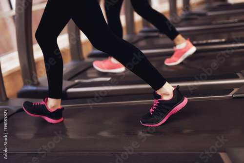Two women running on treadmill at the gym. Fashionable sneakers.