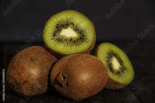 Kiwi fresh whole and halves on a black wooden table. Kiwi fruit is useful.