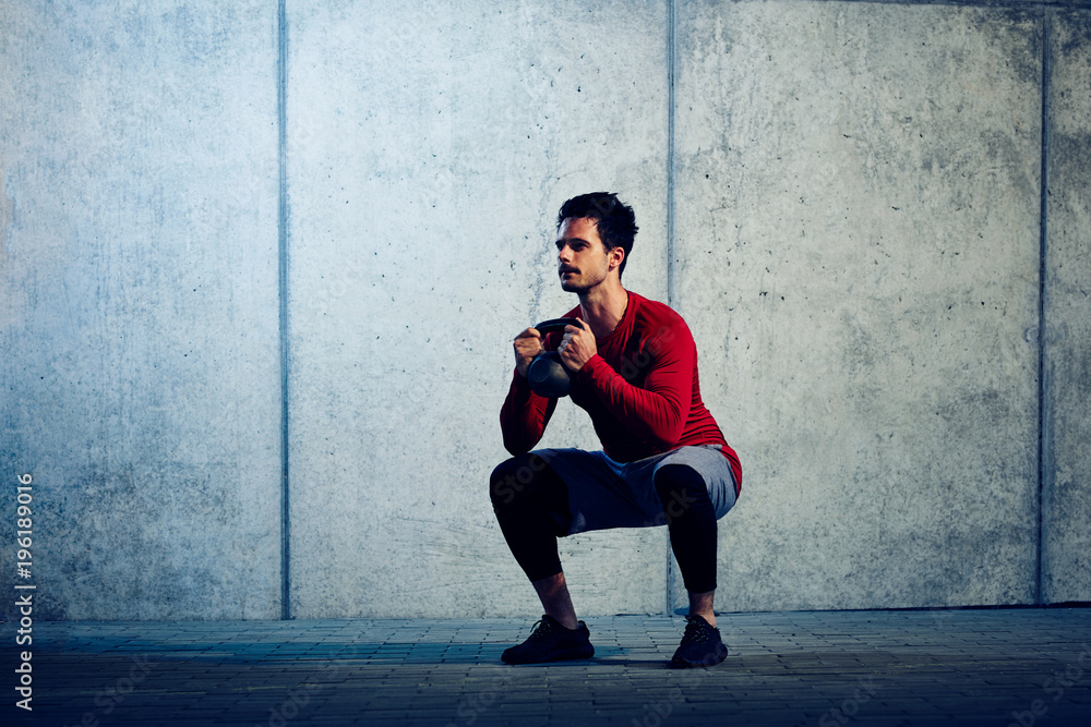 Muscular young man doing kettlebell squats during workout