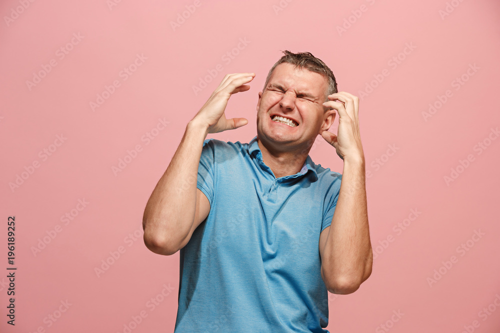 Fototapeta premium The young emotional angry man screaming on pink studio background