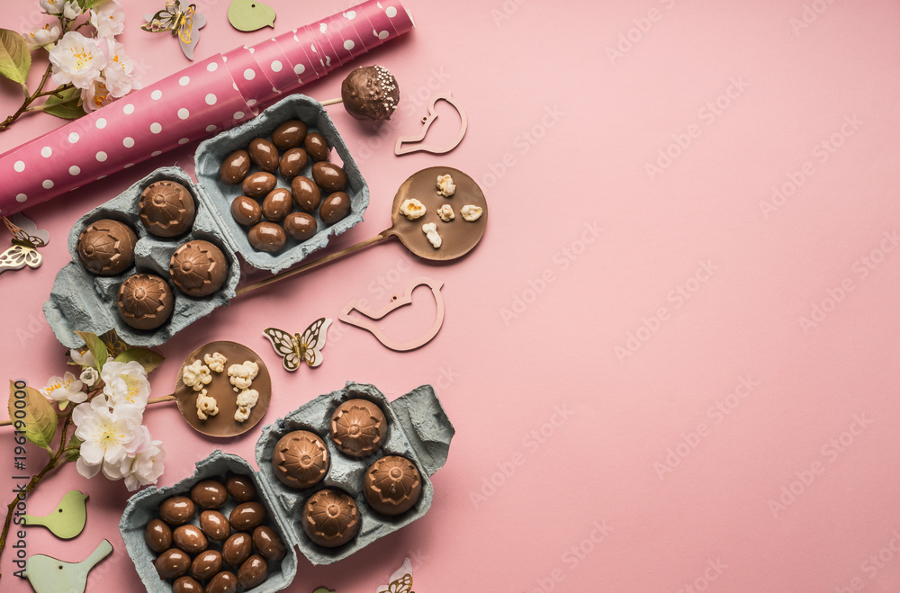 Easter composition with chocolate eggs and holiday decorations, wrapping paper, and sweets on pink background, space for text, border Easter composition with chocolate eggs and holiday decorations, wrapping paper, and sweets on pink background, space for text, border