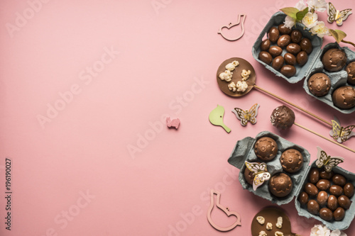 Easter composition with chocolate eggs and holiday decorations on pink background, space for text border