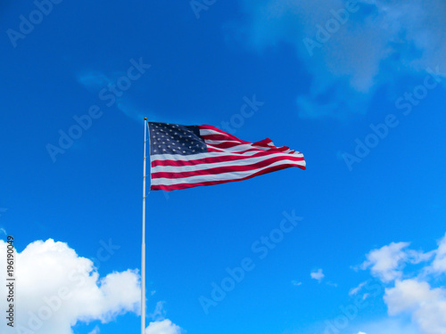 USA flag on the clear blue sky background.  Bright sunny view of a high flagpole with a flag in the wind.