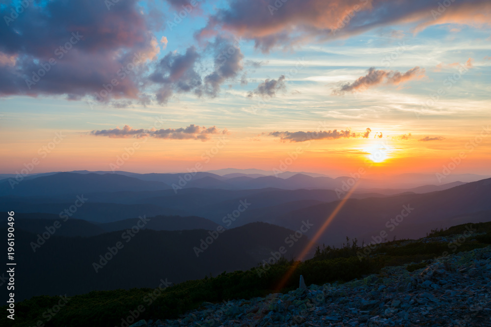 Orange sun descends on the horizon above the mountain ranges Orange sun descends on the horizon above the mountain ranges