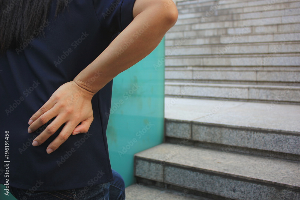 young woman with lower back pain while walking up the stairs, health  concept Stock Photo | Adobe Stock