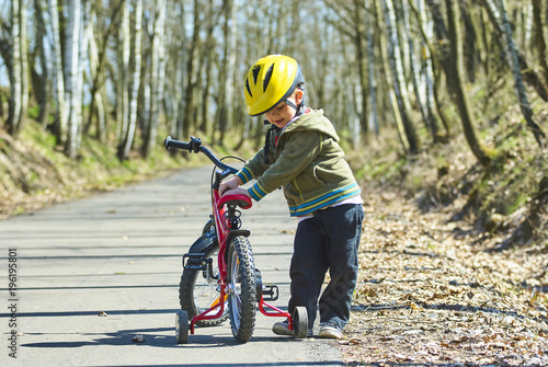 Little child boy cycling on bicycle in green park outdoor in spring. A child is riding a children's bike with support training wheels wearing safety helmet 