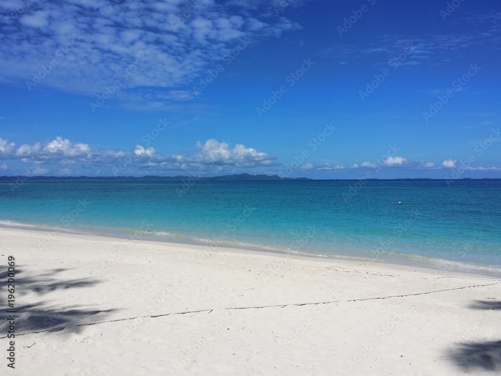 Ocean view of blue sky, beautiful clouds and pacific crystal turquoise water beside a tropical island with powdery white sand . Palambak island, Indonesia