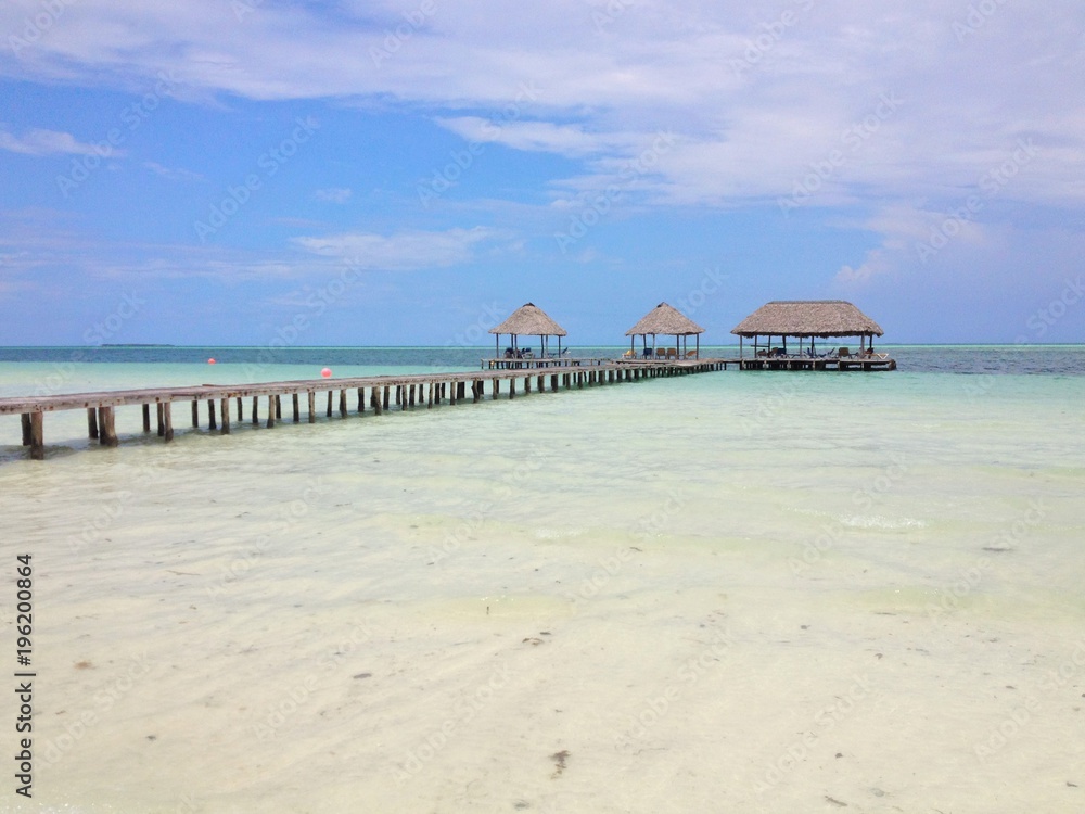 Naklejka premium Blue sky and white clouds over a tropical pier that stretched out in to the crystal blue sea. Cayo Guilermo , Cuba