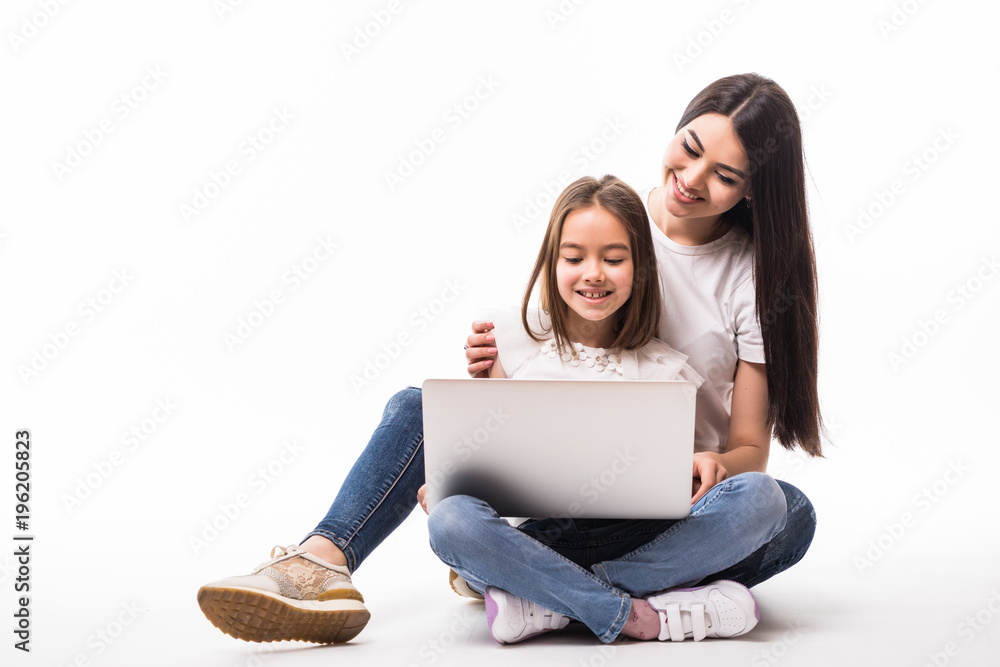 Mother and smile daughter watching on laptop screen sitting on floor on white background