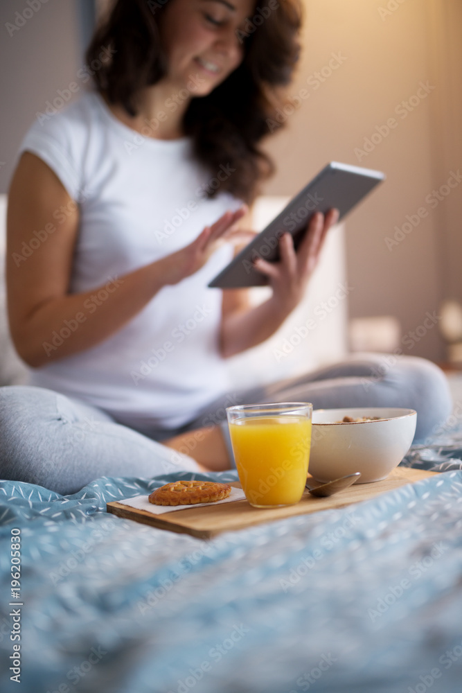 Close up of dinner on the bed in focus in front of a pretty smiling woman while touching a tablet. Close up of dinner on the bed in focus in front of a pretty smiling woman while touching a tablet.