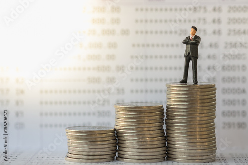Business, money and saving concept. Businessman miniature figure standing on stack of silver coins on bank passbook.