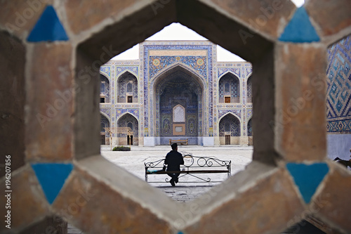 Sher Dor Madrasah. Man is sitting on a bench in the courtyard of Sherdor Madrassah. Registan square in the center of Samarkand.