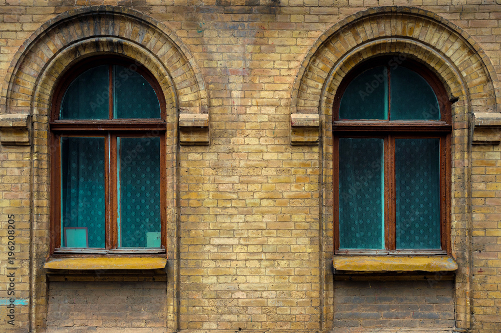 Fototapeta premium Two vintage arched windows in a wall of yellow bricks. Green - the colors of sea wave glass in a maroon dark red wooden frame. The concept of antique vintage architecture in building elements