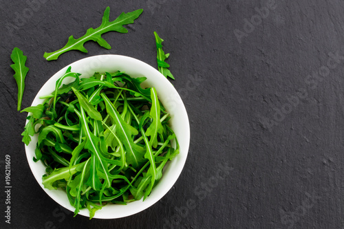 Fresh spring salad with rucola, in bowl on dark stone background with free text space photo