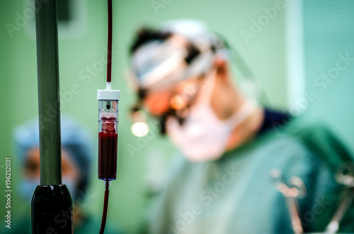 A dropper with donor blood in the operating room. In the background, an operating surgeon.
 photo