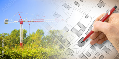 Building a new city - concept image with and drawing an imaginary cadastral map of territory with buildings, fields and roads and a tower crane in a construction site