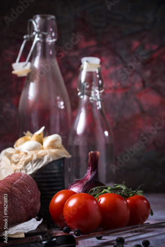 Fototapeta Naklejka Na Ścianę i Meble -  Red tomatoes next to whole pork tenderloin meat on vintage board and garlic