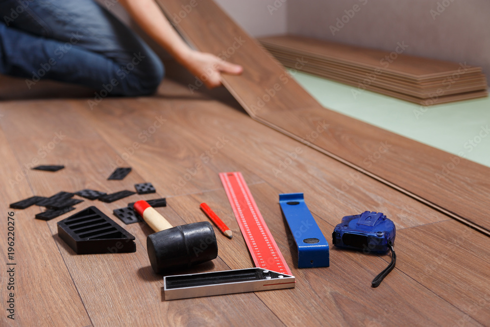 Repairman installing new wooden laminate flooring. On the floor lie different carpenter's tools.
Repairman installing new wooden laminate flooring. On the floor lie different carpenter's tools.