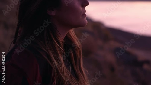 Slowly panning up to young womans face at sunset as she looks off into the distance.
