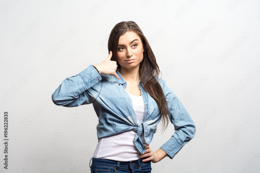 Portrait of a young brunette woman posing in studio, casual style, teenager, showing call me. Lifestyle, fashion and people concept Portrait of a young brunette woman posing in studio, casual style, teenager, showing call me. Lifestyle, fashion and people concept