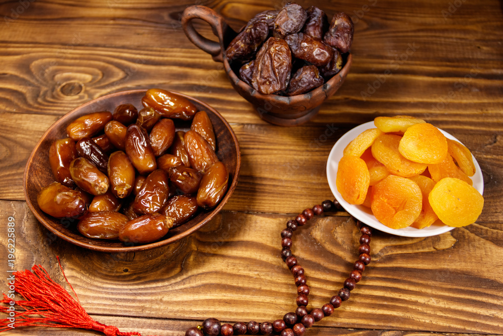 Fototapeta premium Dried apricots and dates fruit with wooden rosary on wooden table