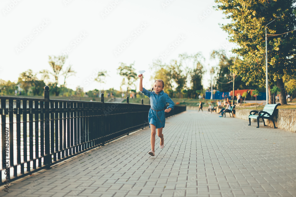 Girl playing, running with toy paper airplane 