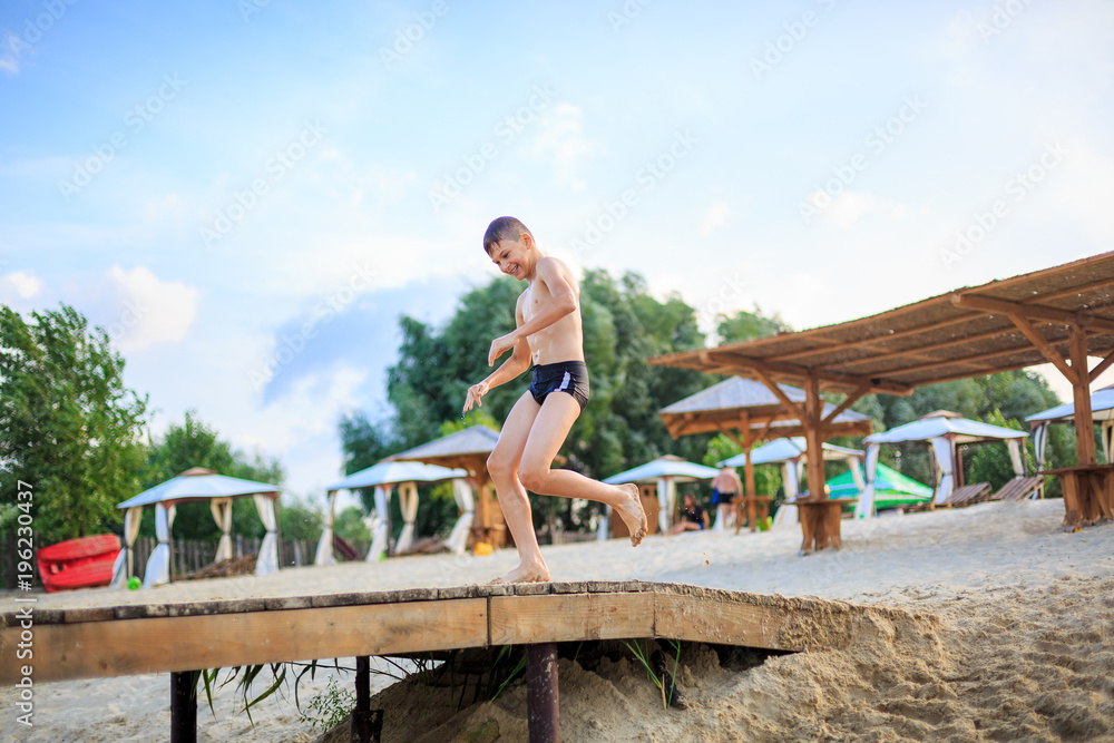 sporty cute young boy jumps very high from pier and having fun on his vacation by the sea