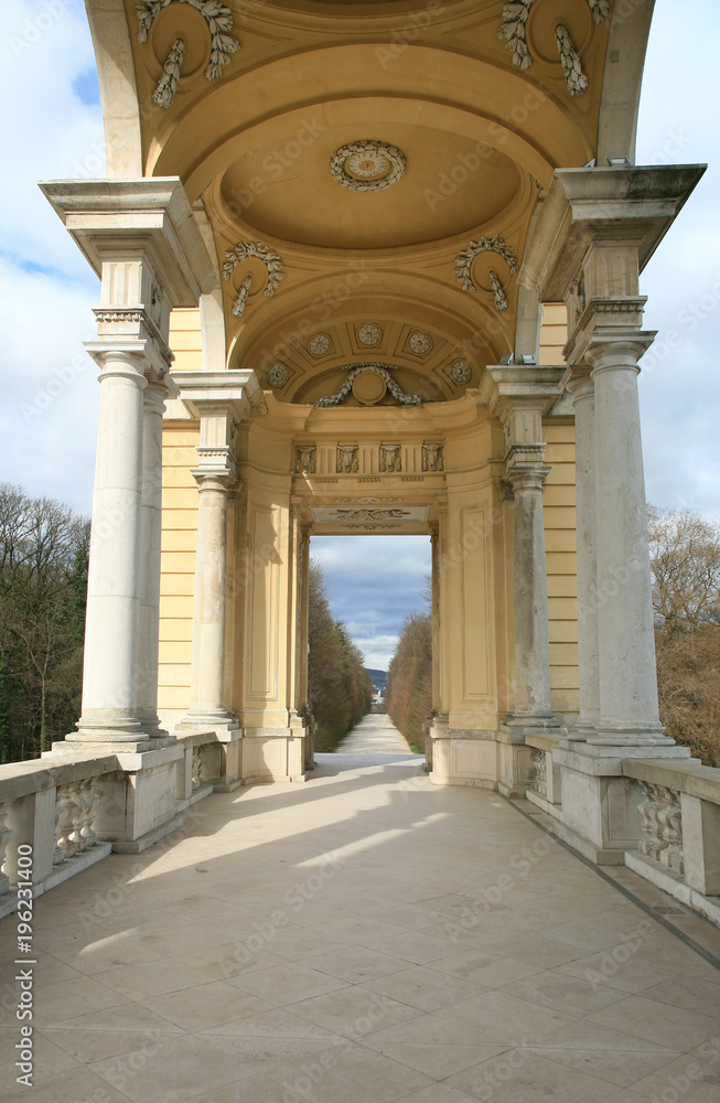 Endlos scheinender Fußweg durch eine offene Säulenhalle in einen Park in Wien