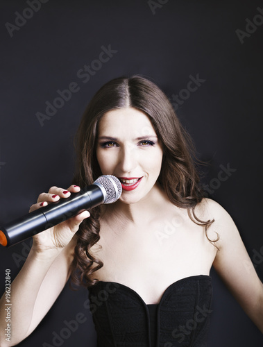 Portrait of beautiful singing woman in black dress with curly hair - isolated on black background