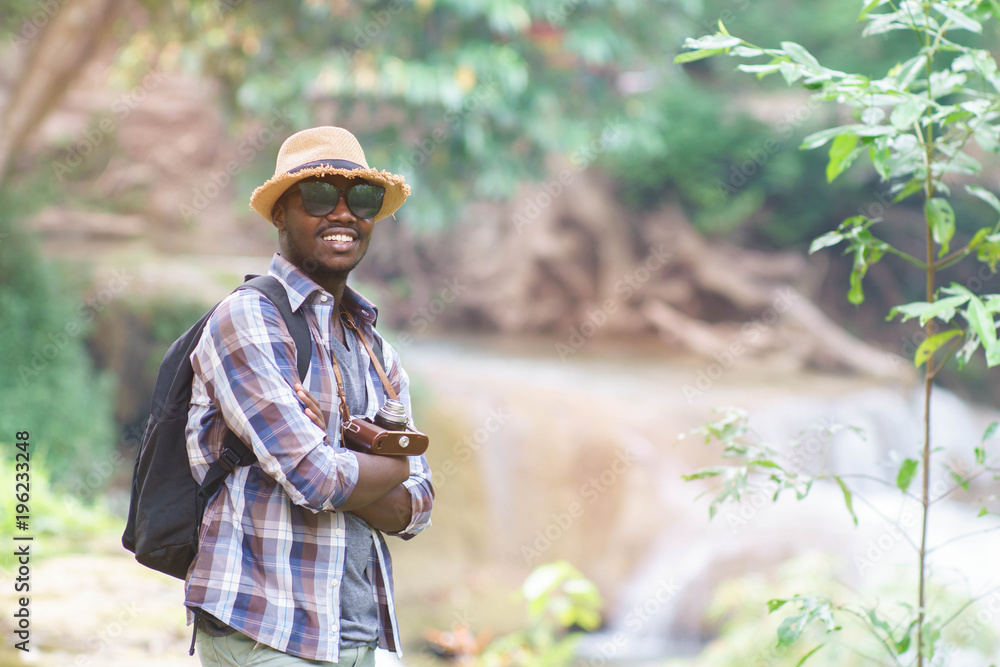 African Man Traveler with backpack standing and holding camera with waterfall background.