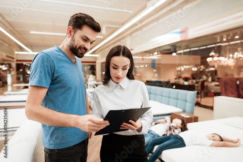 Beautiful girl consultant with confident man make out purchase of mattress in store.