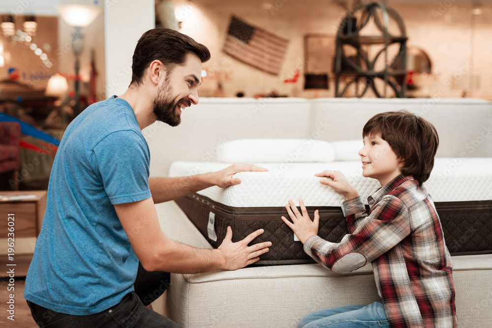 Confident bearded father with small boy choose orthopedic mattress in furniture store. Confident bearded father with small boy choose orthopedic mattress in furniture store.