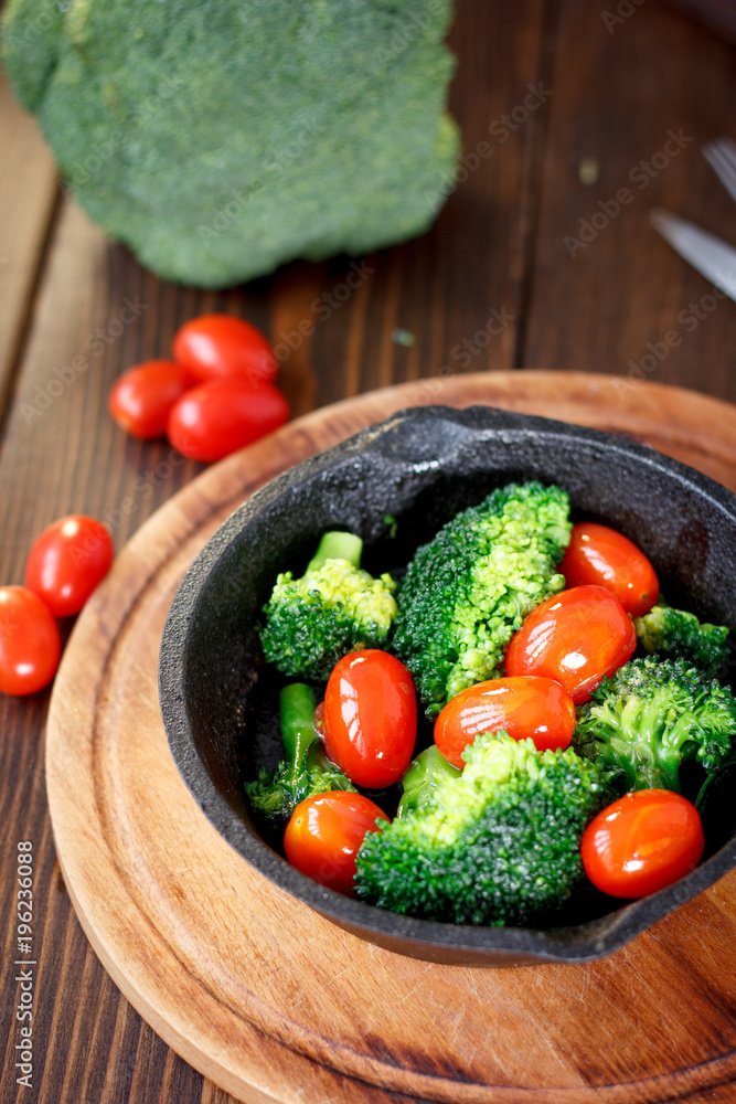 Broccoli cooked with cherry tomatoes inside a frying pan.
