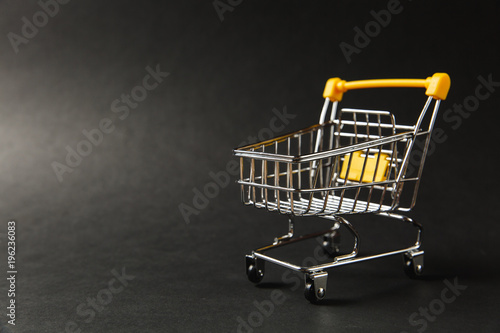 Close up of supermarket grocery push cart for shopping with black wheels and yellow plastic elements on handle isolated on black background. Concept of shopping. Copy space for advertisement