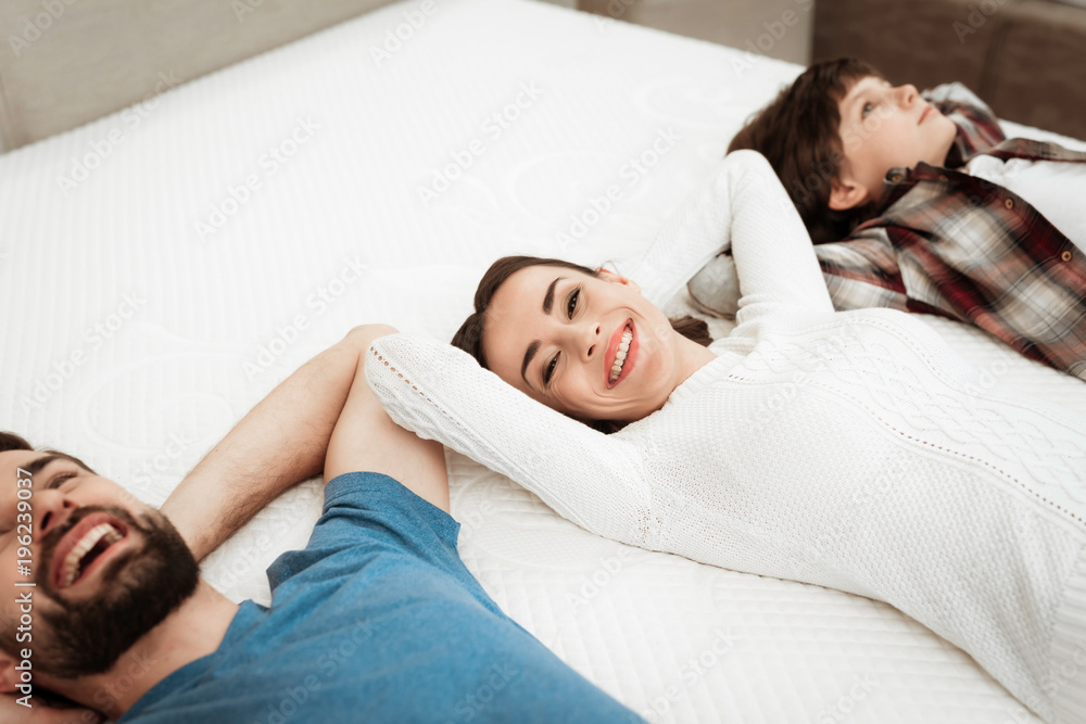 Young happy couple with cute little son lies on bed in mattress store. Young happy couple with cute little son lies on bed in mattress store.