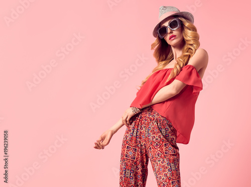 Fashion Young Woman in Summer Stylish Outfit. Wavy Hair, Trendy pants, Luxury Sunglasses, fashion Hat. Fashionable Beautiful Blond Lady. Slim Playful Model Girl Posing in Studio