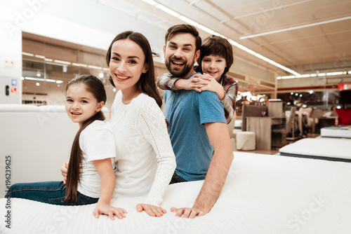 Couple of young parents with little daughter and son are sitting on orthopedic mattress in furniture store. photo