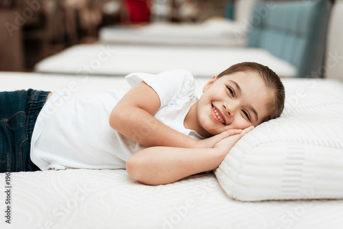 Smiling little girl lies on n orthopedic mattress in a furniture store.