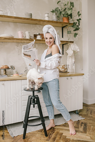 Smiling girl in turban with the cute bulldog in the kitchen reading newspaper