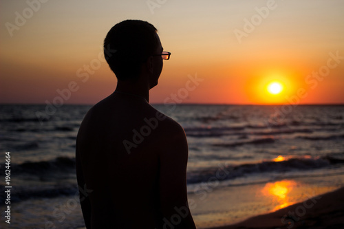 happy young man in glasses at sunset near the sea. silhouette of a man