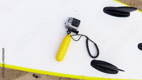 Modern action camera in the case lying on the  of the white surfboard. Camera for shooting in water with a float