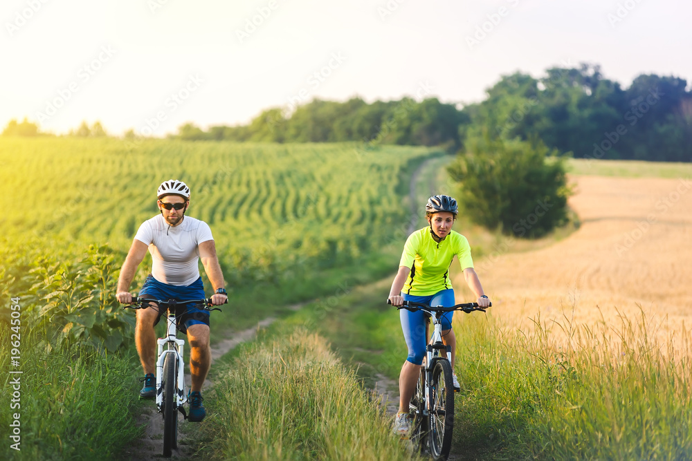 young man and woman are driving their bicycles on their way to the field in the summer. young man and woman are driving their bicycles on their way to the field in the summer.