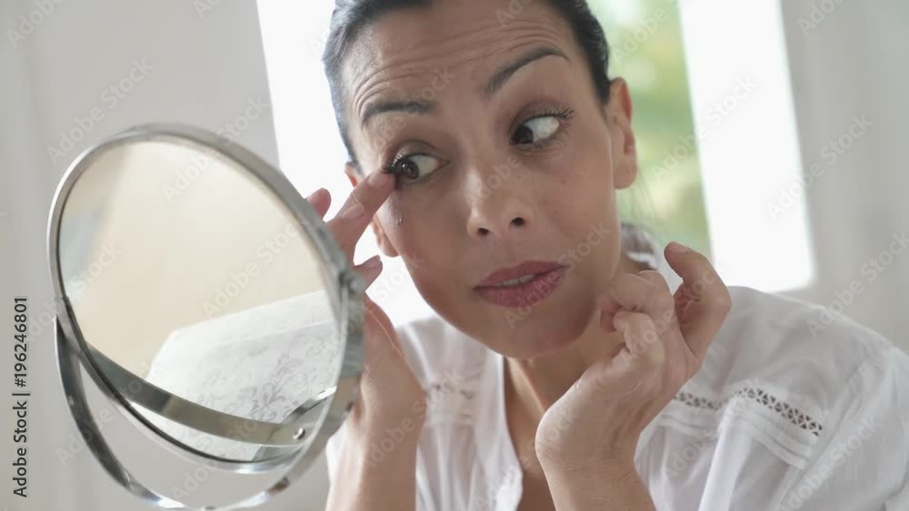 Portrait of brunette woman looking at her face in mirror Portrait of brunette woman looking at her face in mirror