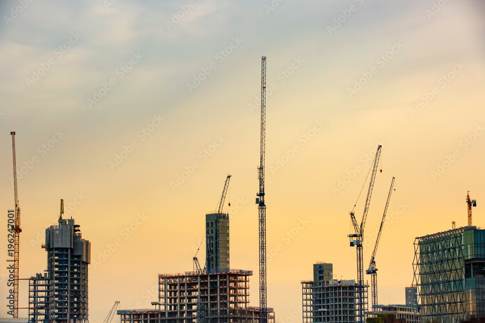 New skyscrapers under construction with tall cranes against yellow sky. Construction business and industry, urbanisation, urban sprawl real estate bubble concept, background with copy space. 